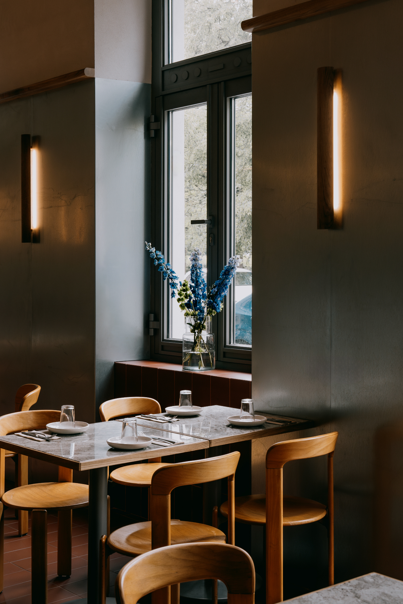 Wnętrze restauracji śniadaniowej Pora na Kazimierzu — drewniane krzesła, marmurowe stoliki i błękitne kwiaty w oknie